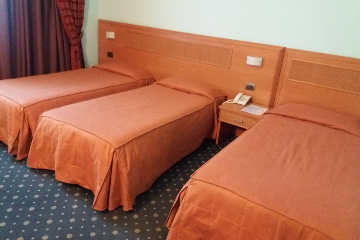 A hotel room with three single beds, a bedside table with a phone, and a curtain.