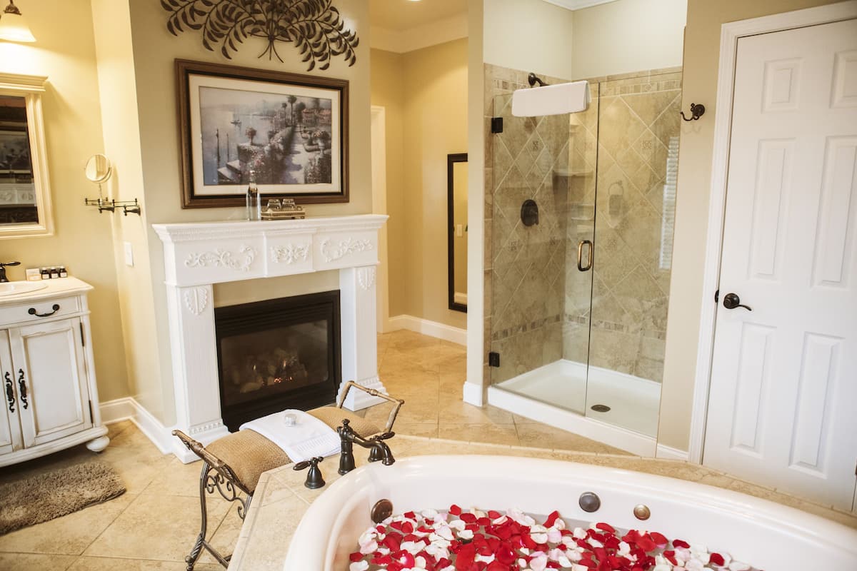 A bathroom with a bathtub, shower, fireplace, and a framed picture on the wall.