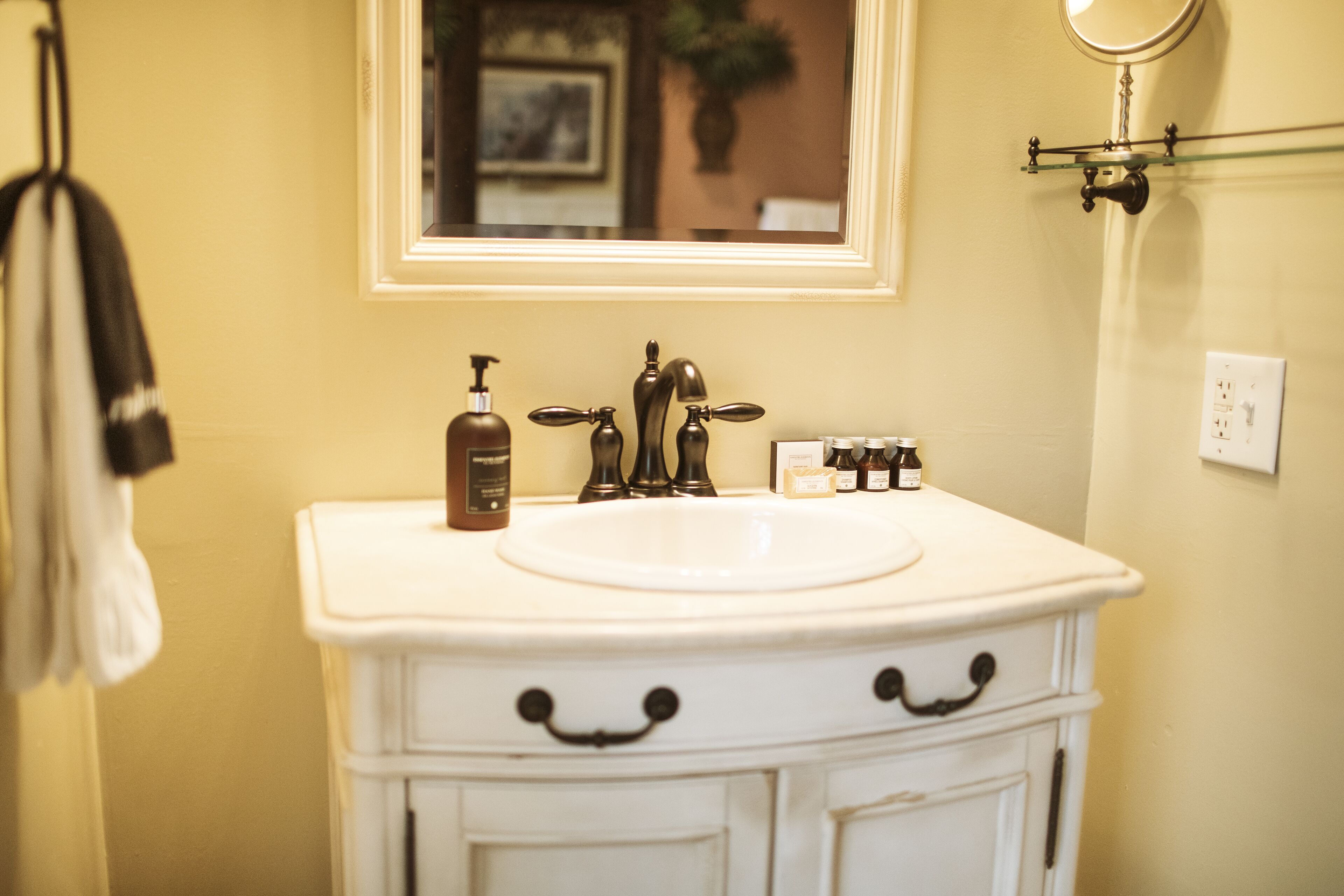 A bathroom with a white sink, two faucets, a mirror, and a towel rack.