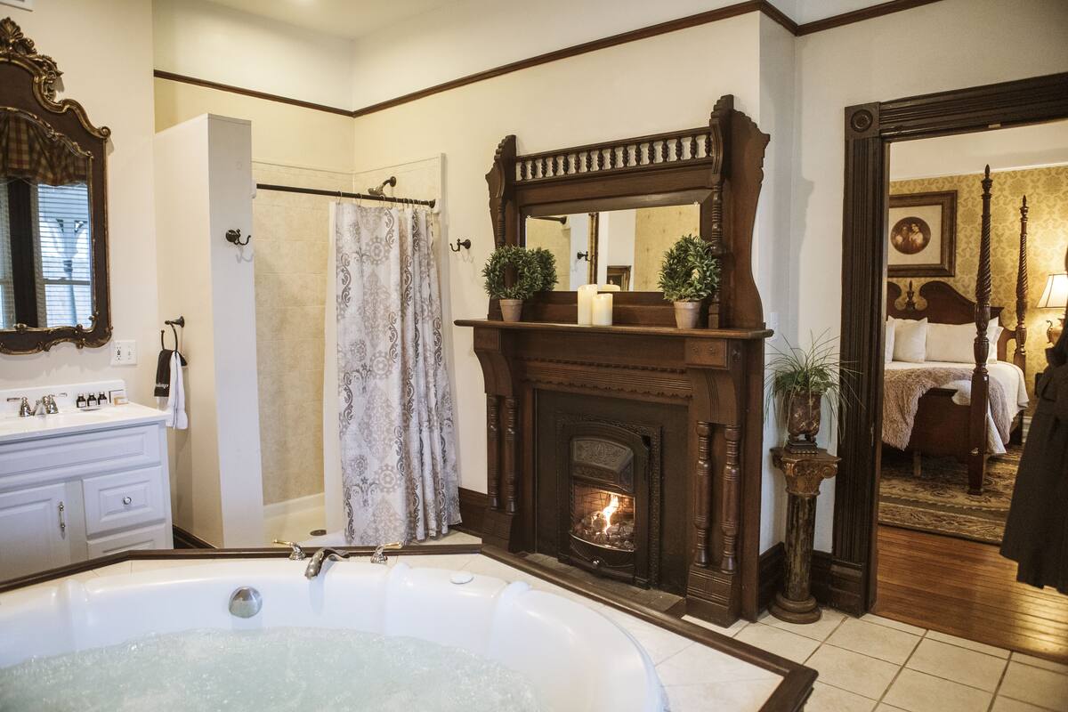 A bathroom with a large bathtub, a fireplace, and a mirror above it.