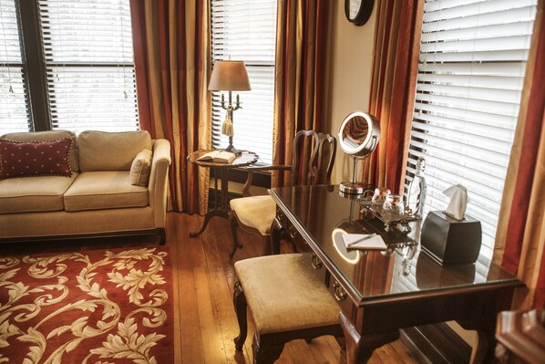 A cozy living room with a sofa, a coffee table, a side table with a lamp, a mirror, and a desk with a lamp. - Biltmore Village Inn B&B (Asheville)