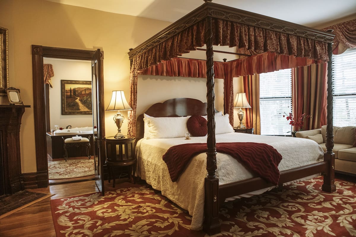 A four-poster bed with a canopy, a sitting area with a sofa, a mirror, and a painting on the wall.