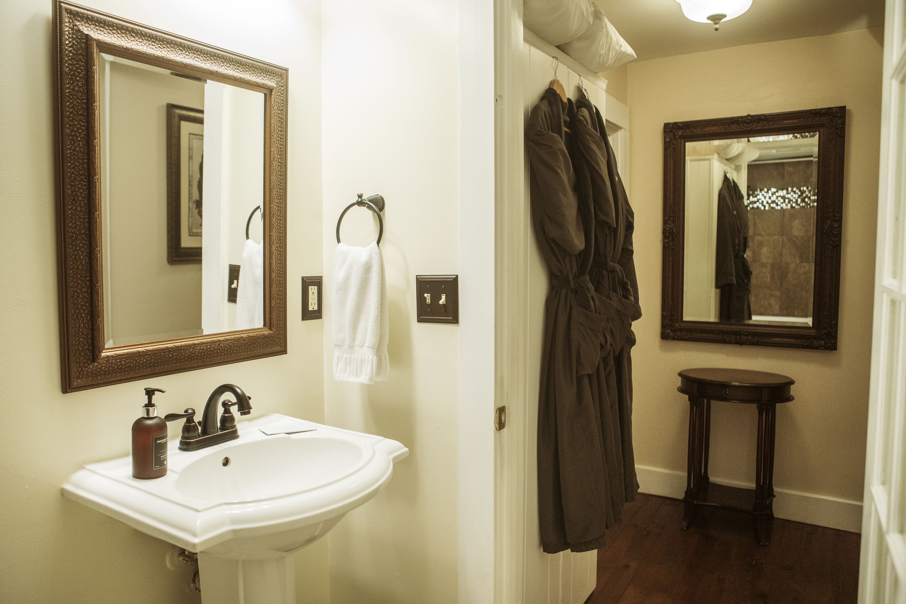 Une salle de bain avec un lavabo blanc, un grand miroir et un porte-peignoir.