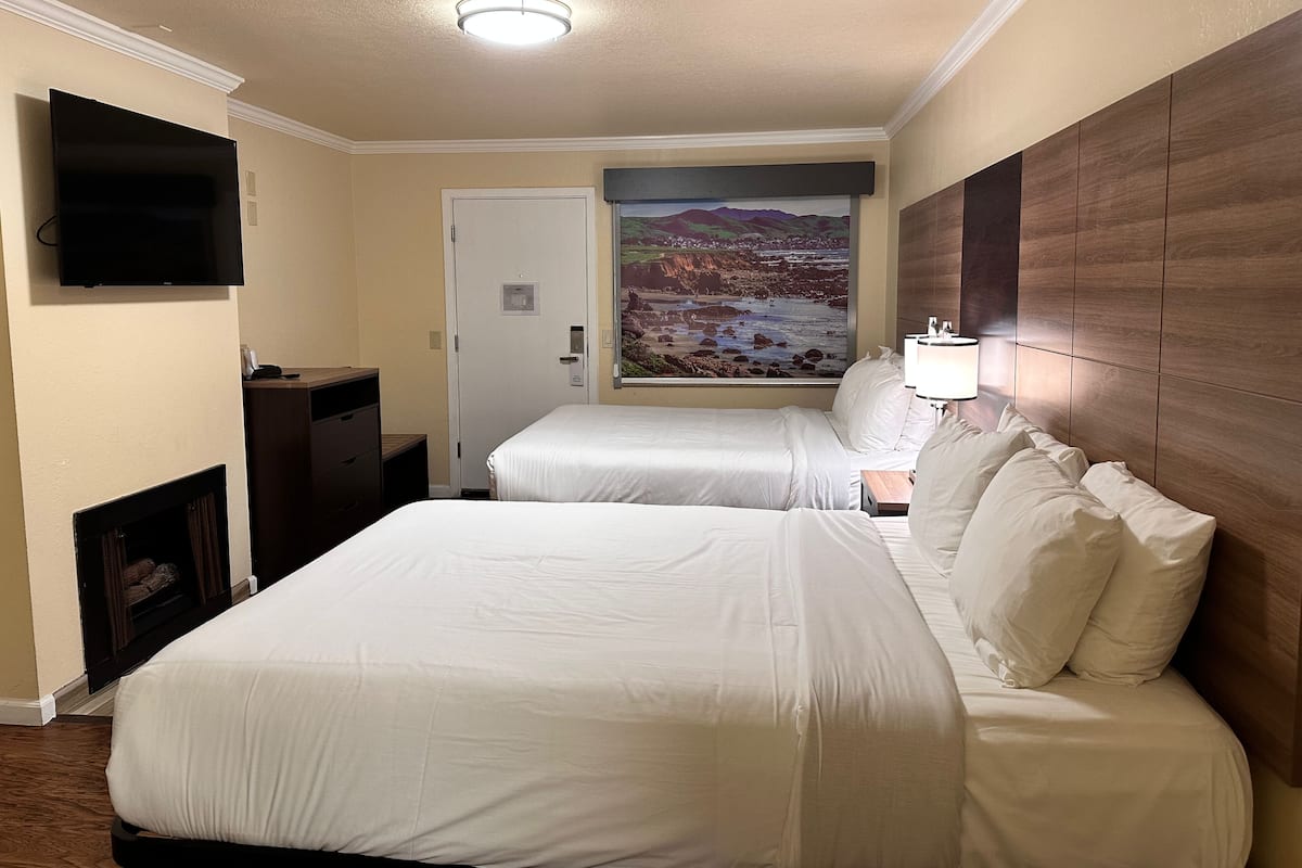 A hotel room with two beds, a flat-screen TV, a painting of a landscape, and a wooden headboard.
