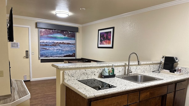 A kitchen with a granite countertop, stainless steel sink, and wooden cabinets. - Beachwalker Inn and Suites (Cayucos)