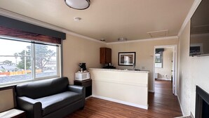 A modern kitchen with a built-in island, a black leather sofa, and a window with a view of the outside. - Beachwalker Inn and Suites (Cayucos)