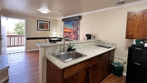 A modern kitchen with a granite countertop, stainless steel sink, and wooden cabinets. - Beachwalker Inn and Suites (Cayucos)