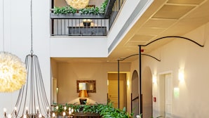 Un hall d’hôtel agrémenté d’un lustre, d’une table ornée de plantes, d’un miroir et d’un balcon verdoyant.