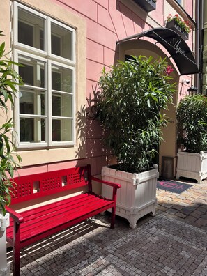 A red bench outside a building with a pink facade, large windows, and potted plants.