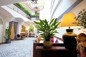 Um amplo átrio com teto alto, um candelabro, uma planta em vaso, um abajur e uma área de estar com mesa e cadeiras.