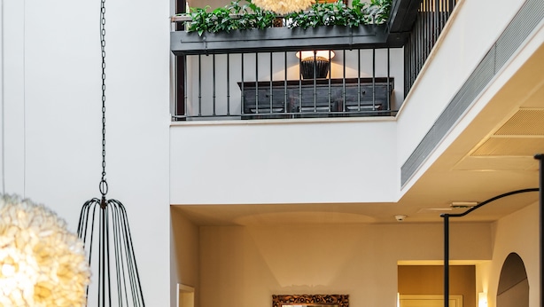 Un intérieur à plusieurs niveaux agrémenté d’un lustre, d’un grand miroir et de plantes vertes sur les balcons.