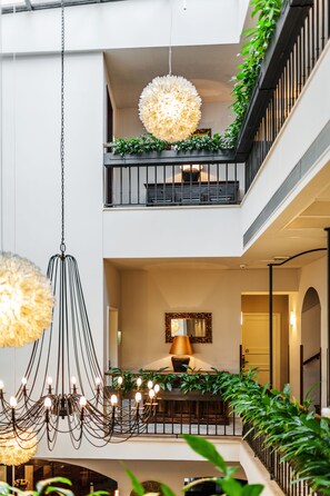 A multi-level interior with a chandelier, a large mirror, and greenery on balconies. - Hotel Residence Agnes (Prague)