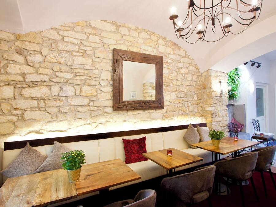 Un muro in pietra con uno specchio, tavoli di legno, sedute imbottite e un lampadario.