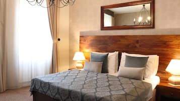 A hotel room with a wooden headboard, a large bed with patterned bedding, two bedside lamps, and a mirror above the bed.