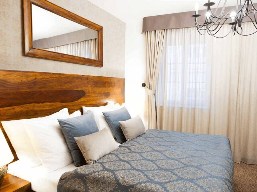 Quarto de hotel com cabeceira de madeira, um espelho grande, um candelabro e uma cama com roupa de cama estampada.