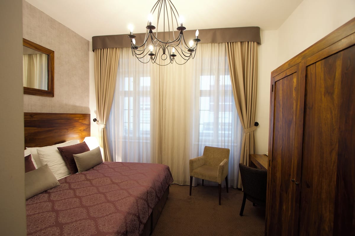 Une chambre d’hôtel avec un grand lit, une chaise, une armoire en bois et un lustre.