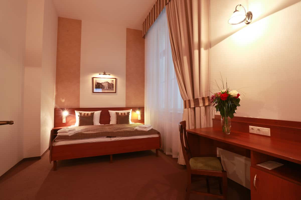 Habitació d'hotel amb un llit, una taula de nit, una cadira, escriptori i un quadre penjat a la paret.