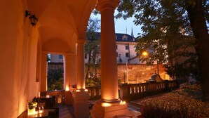 Eine Terrasse mit Esstisch, Säulen und Blick auf ein Gebäude mit einem Turm.