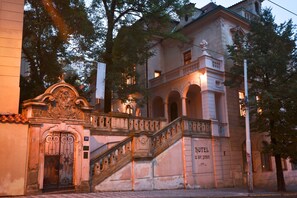 Um edifício histórico com uma entrada imponente, uma escadaria e uma placa indicando que é um hotel.