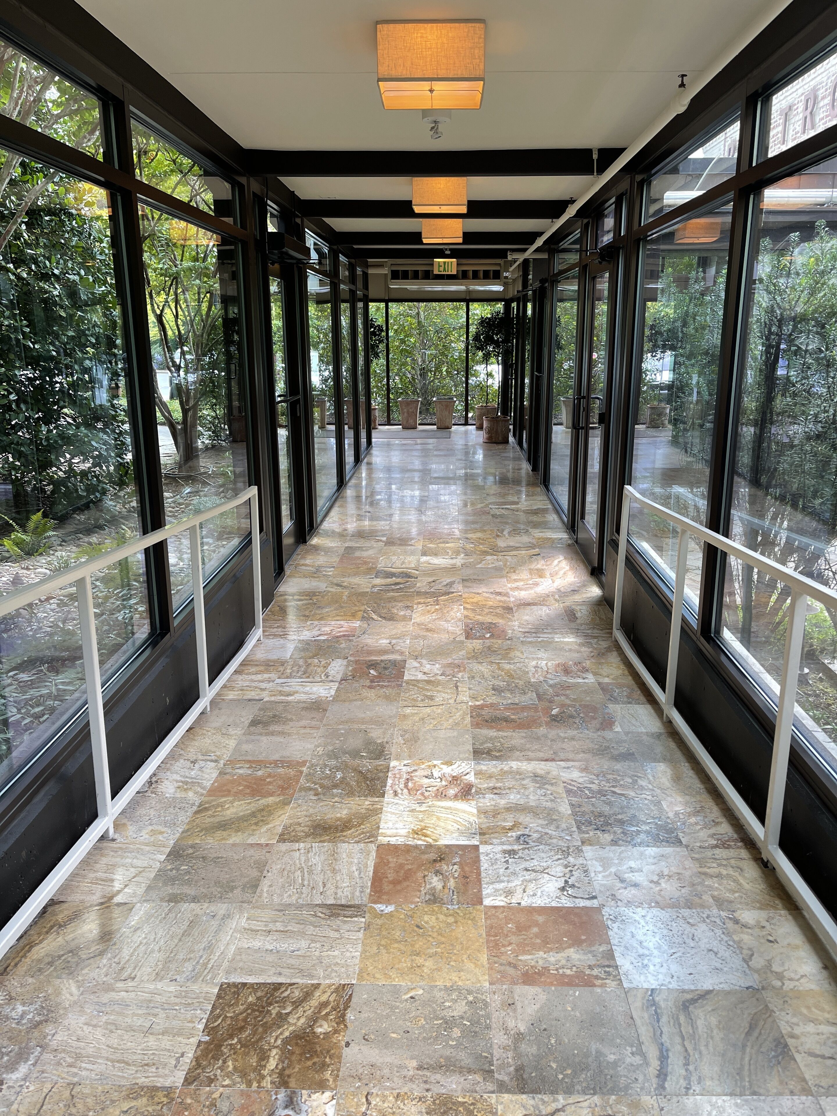 A corridor with large windows, a marble floor, and an exit sign.