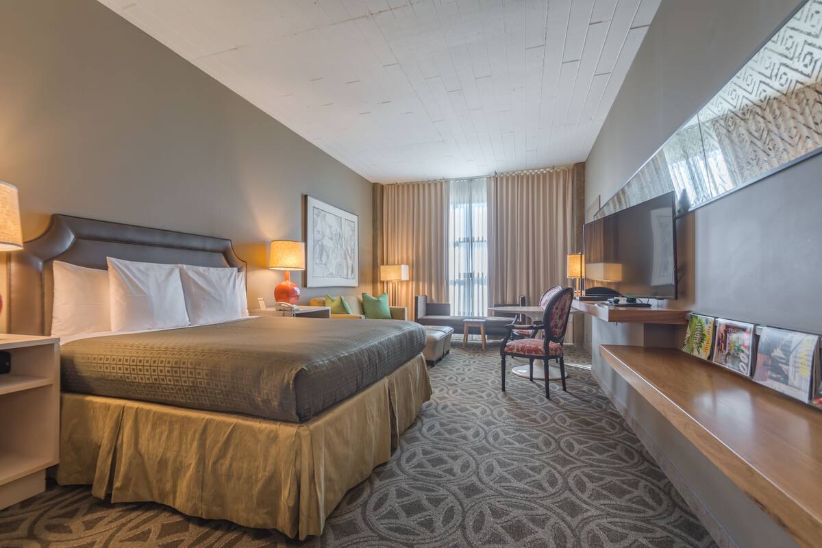 A hotel room with a large bed, a desk, a chair, a television, and a window with curtains.
