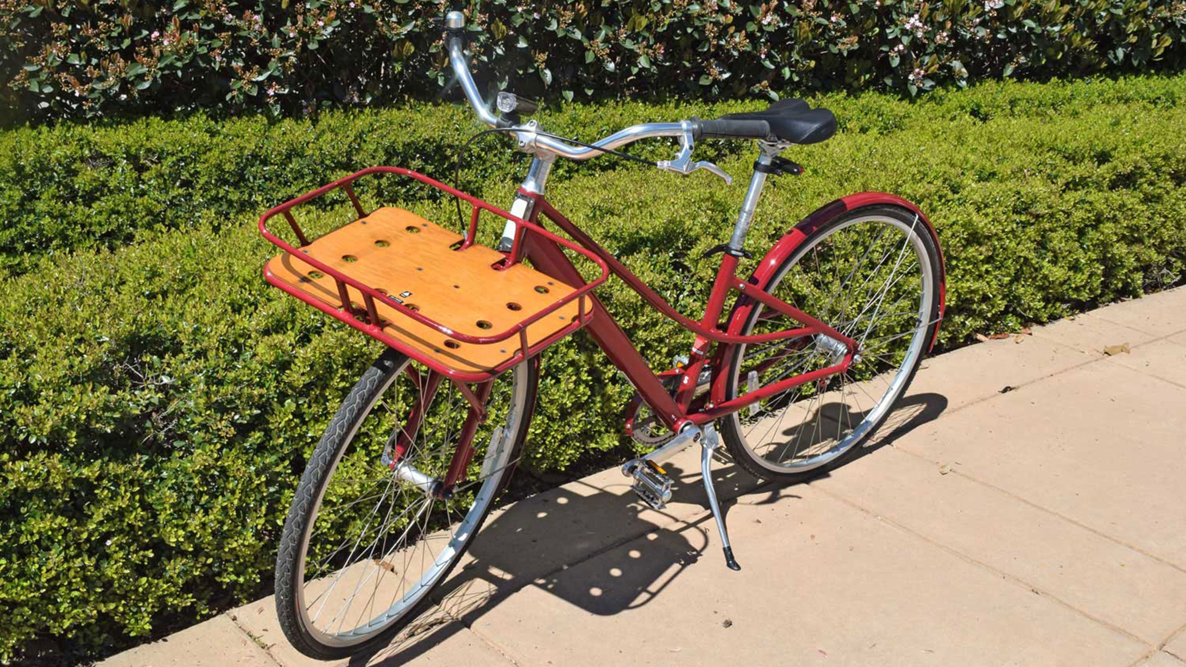 Een rode fiets met een houten zadel en een mandje, geparkeerd op een verhard pad.