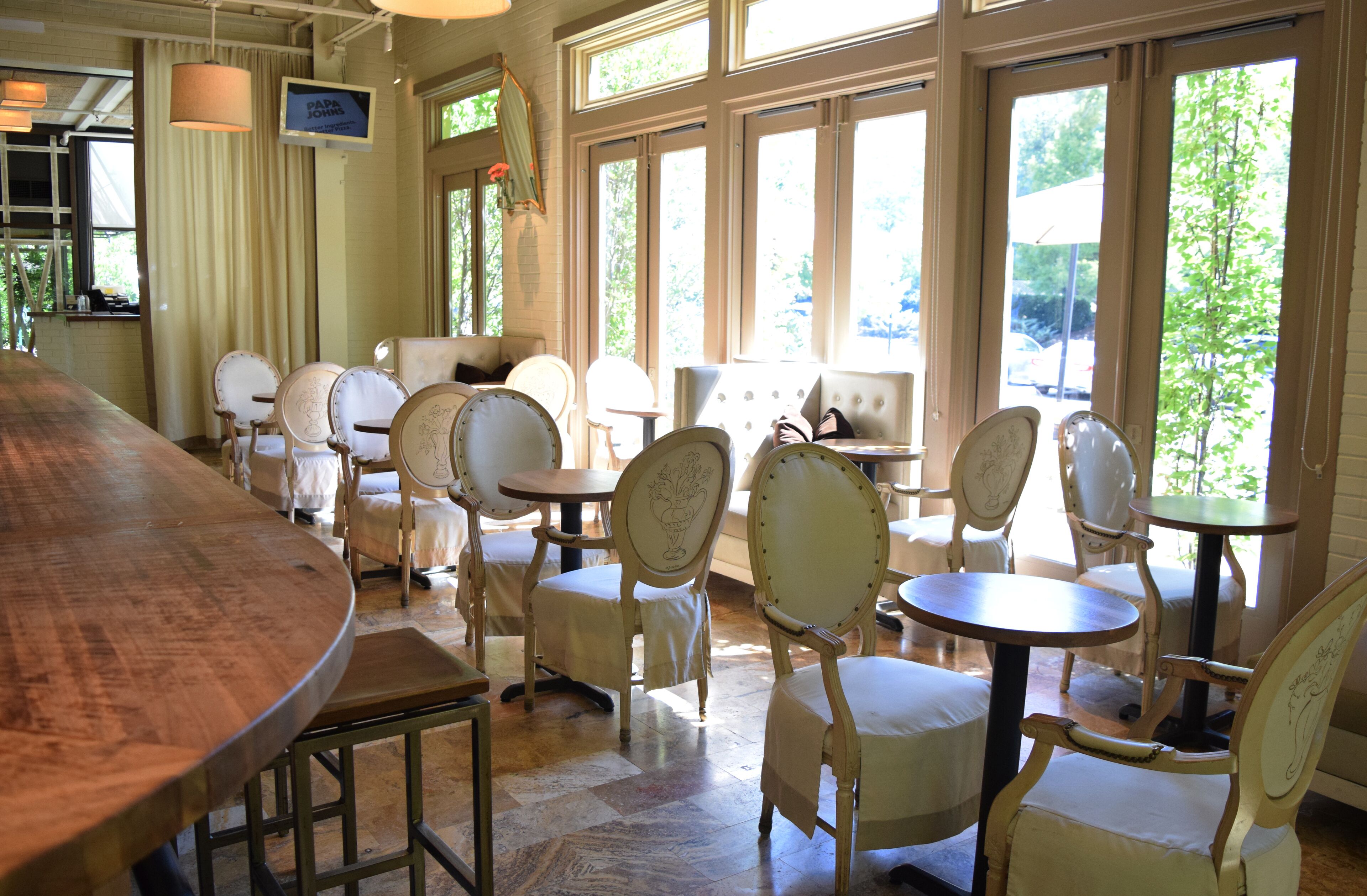 A restaurant with a long wooden bar, several round tables, and white upholstered chairs.