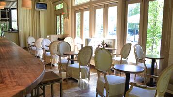 A restaurant with a long wooden bar, several round tables, and white upholstered chairs.