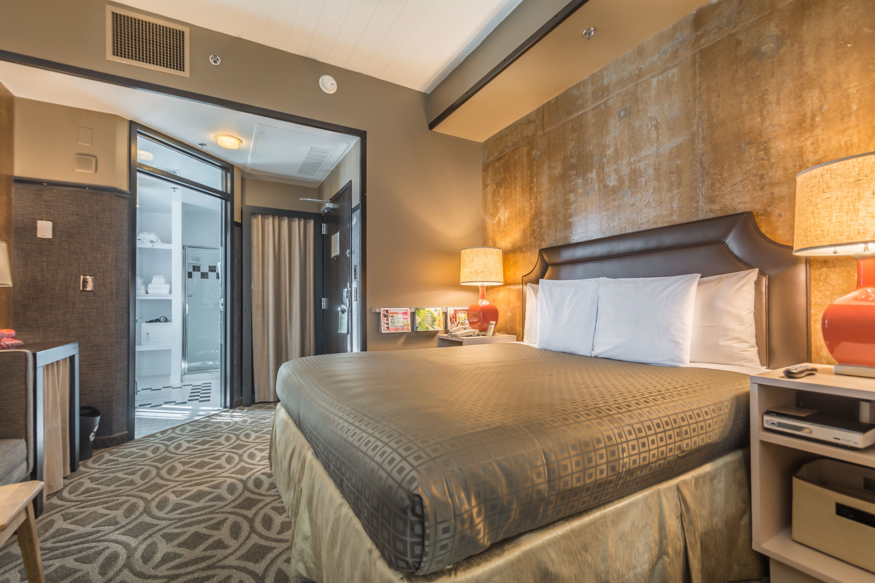 A hotel room with a large bed, a desk, a lamp, and a view of the hallway.