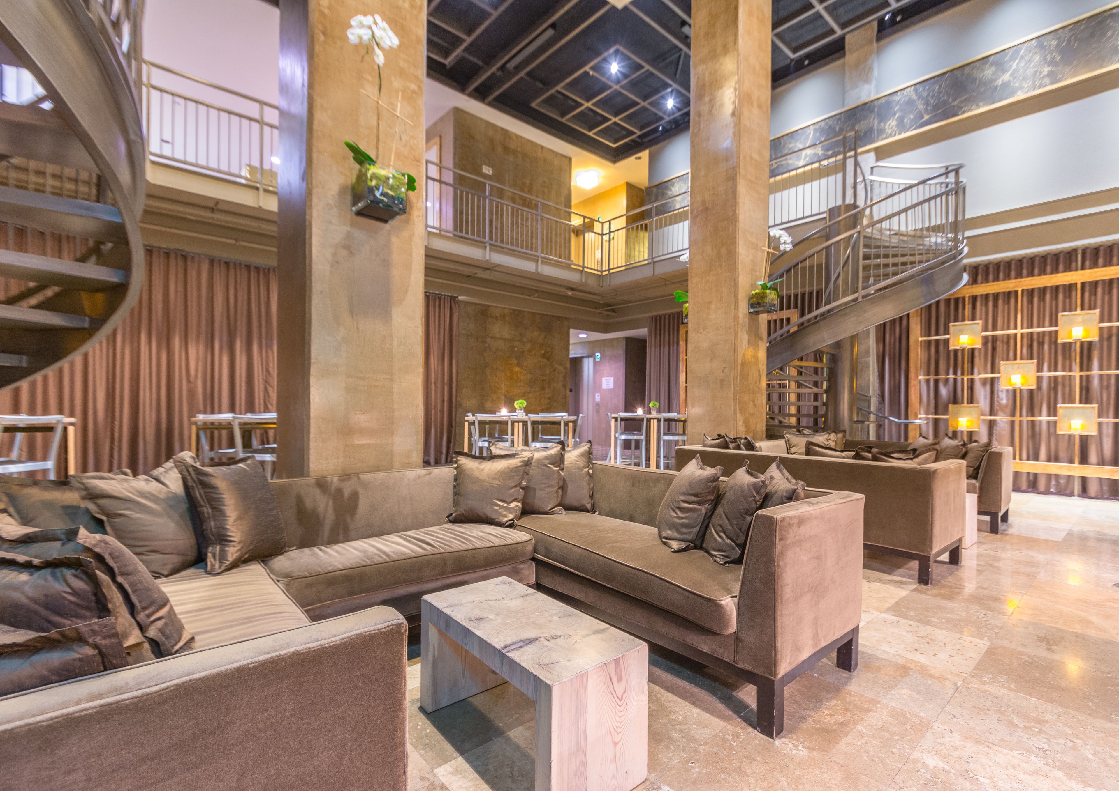 A spacious lobby with a modern design, featuring a large seating area with sofas and a coffee table, a staircase, and a decorative plant.