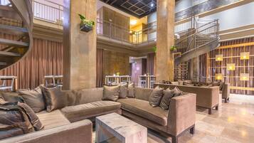 A spacious lobby with a modern design, featuring a large seating area with sofas and a coffee table, a staircase, and a decorative plant.