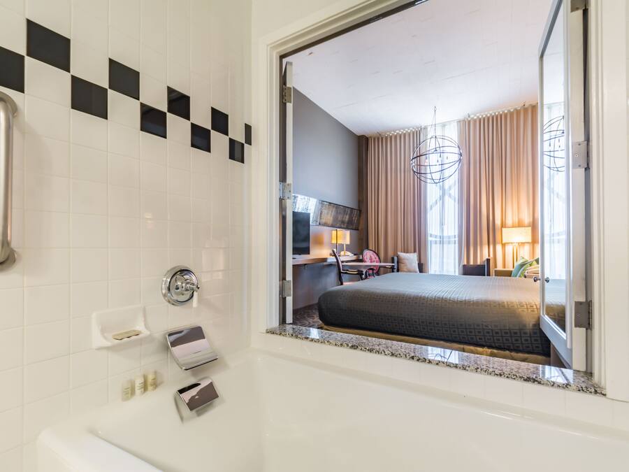 Habitación de hotel con una cama grande, un baño con bañera y un escritorio con silla.
