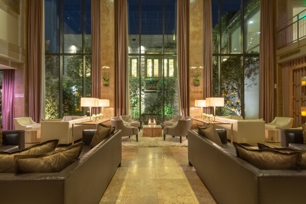 A spacious lobby with a central seating area, large windows, and a view of greenery outside.