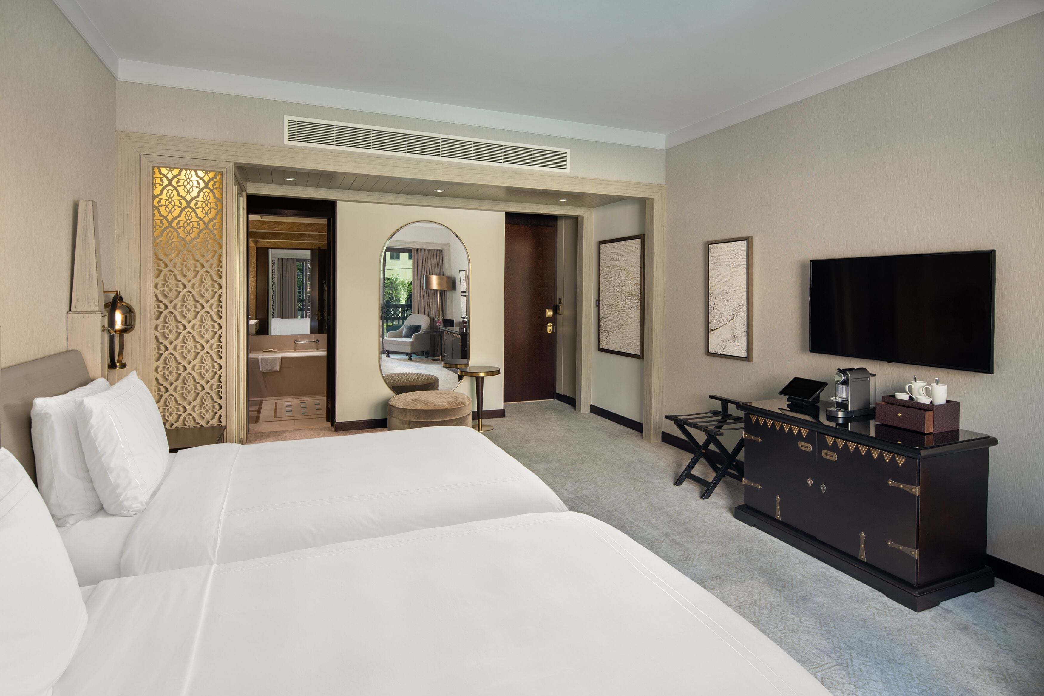 A hotel room with two beds, a desk, a TV, and a minibar.