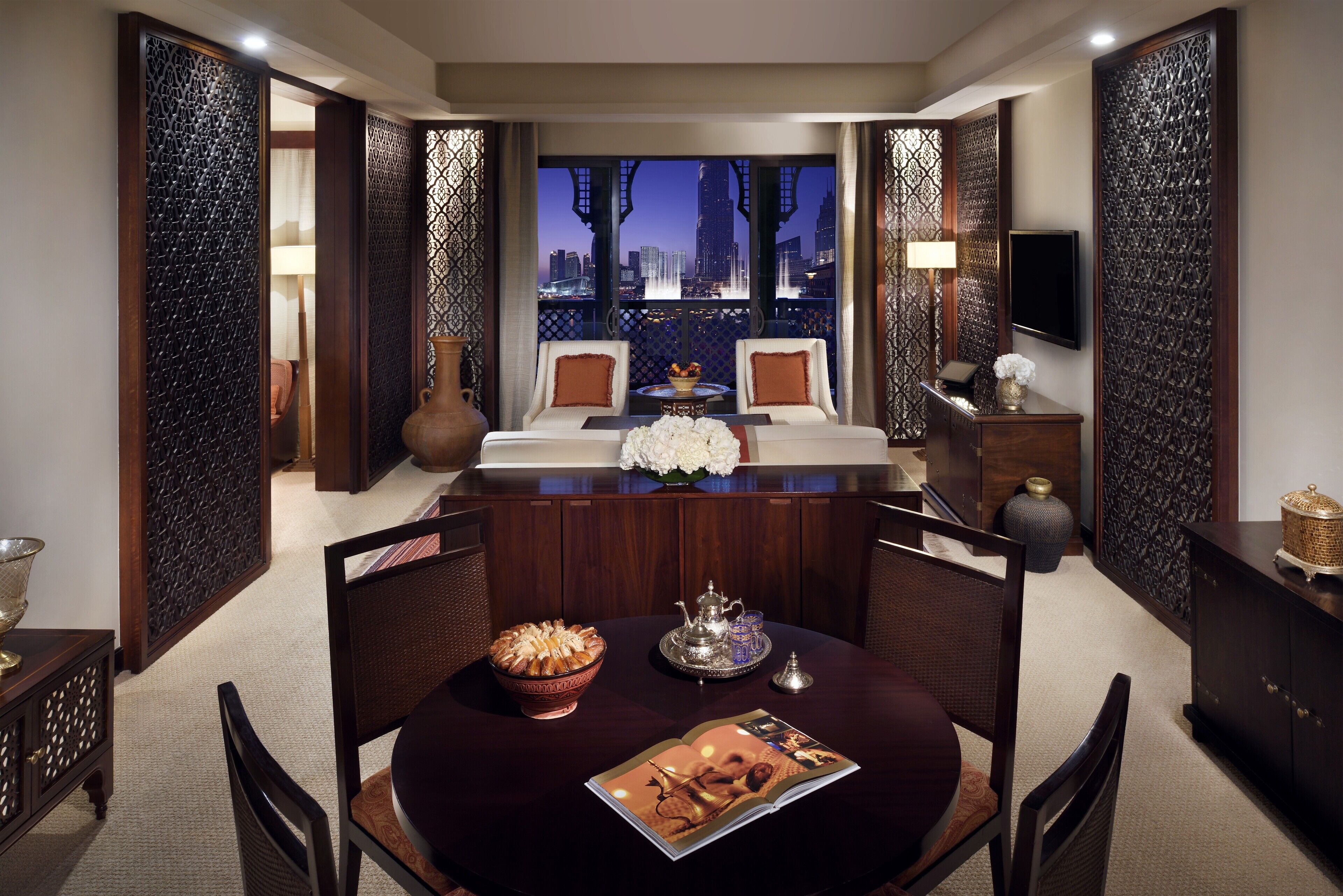 A modern hotel room with a dining area, a large window with a city view, and traditional decor elements.