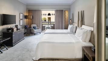 A hotel room with a large bed, a desk with a computer, a TV, and a balcony with curtains.