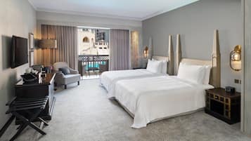 A hotel room with a large bed, a desk with a laptop, a chair, and a view of a pool and buildings through the window.