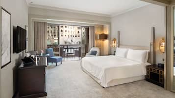 A hotel room with a large bed, a desk with a laptop, a chair, and a balcony with a view of buildings.