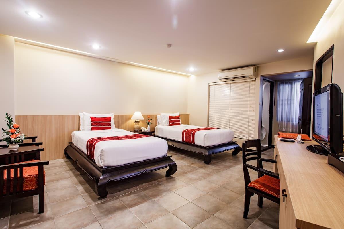A hotel room with two beds, a desk, a chair, and a television.
