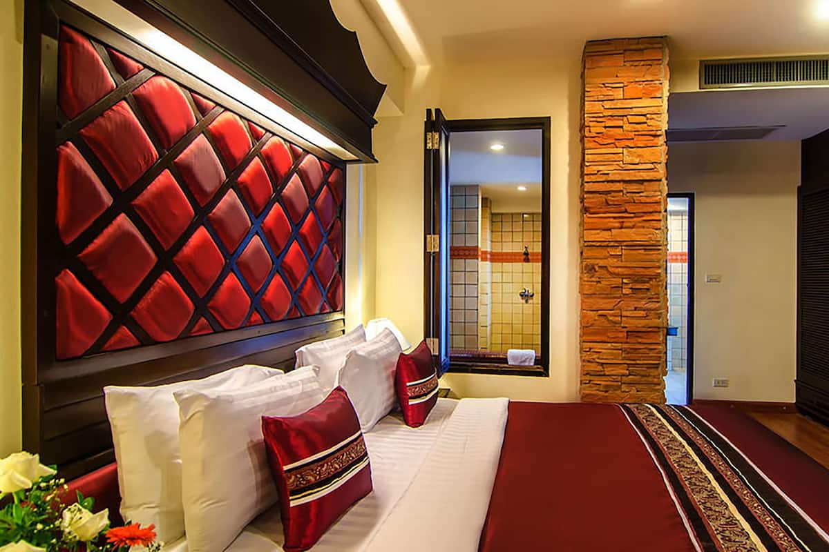 A hotel room with a large bed, a red headboard, a stone accent wall, and a view of the bathroom.