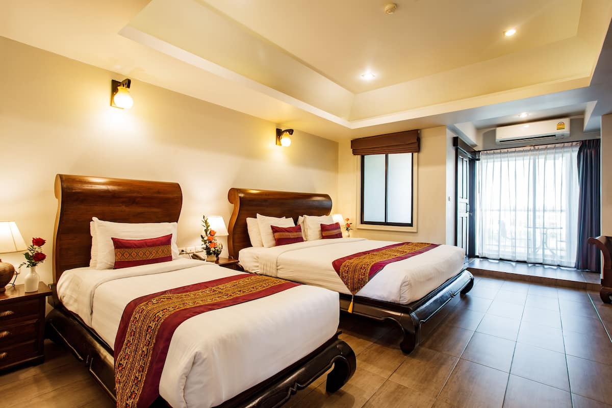A hotel room with two beds, wooden headboards, white bedding, and a large window with curtains.