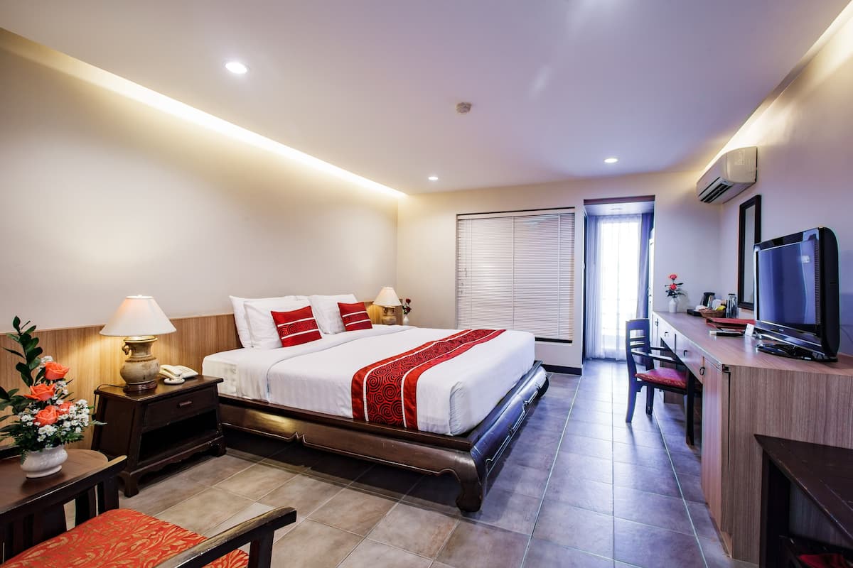 A hotel room with a bed, bedside table with a lamp, a desk with a computer, a TV, and a chair.