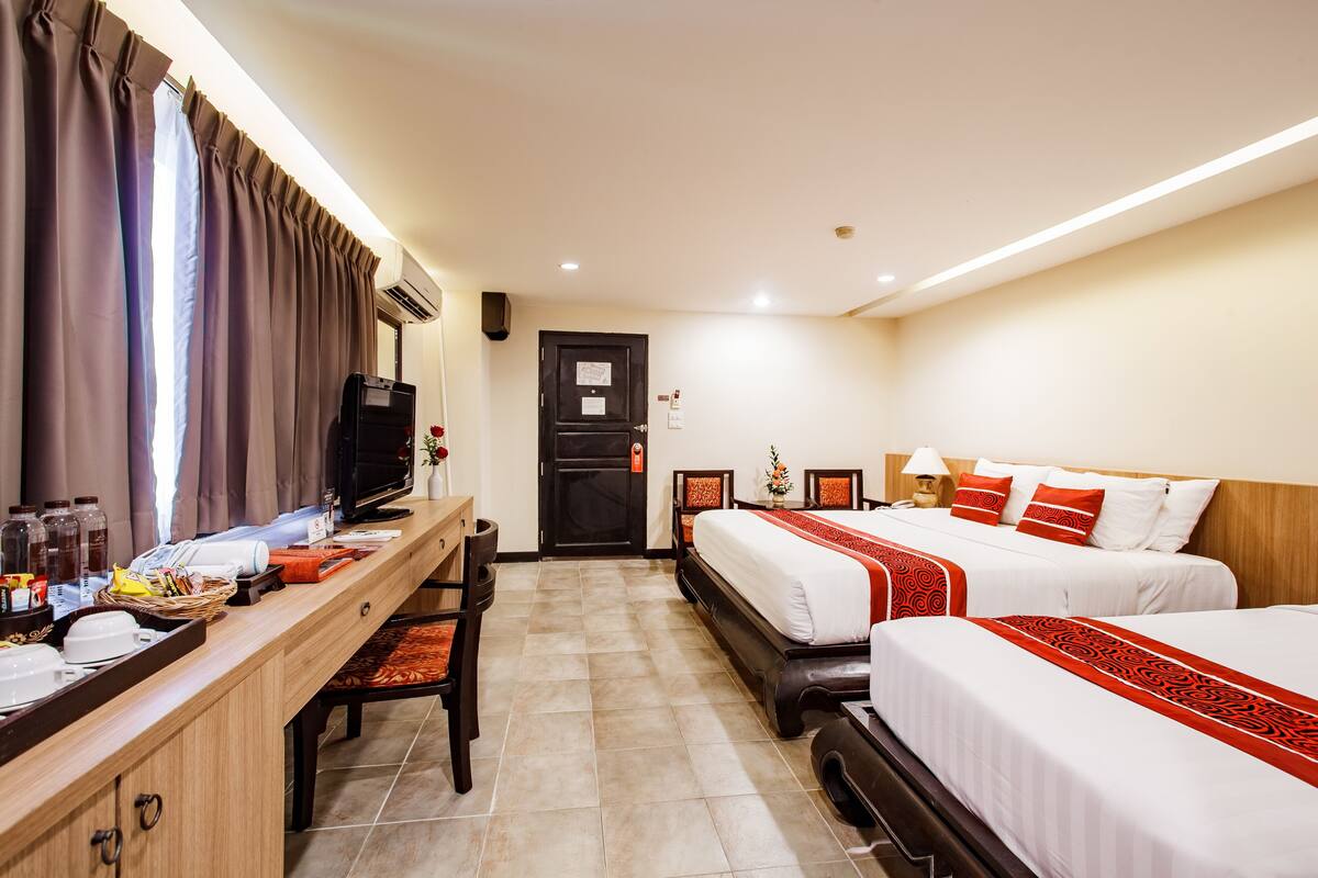 A hotel room with two beds, a desk, a television, and a door with a map.