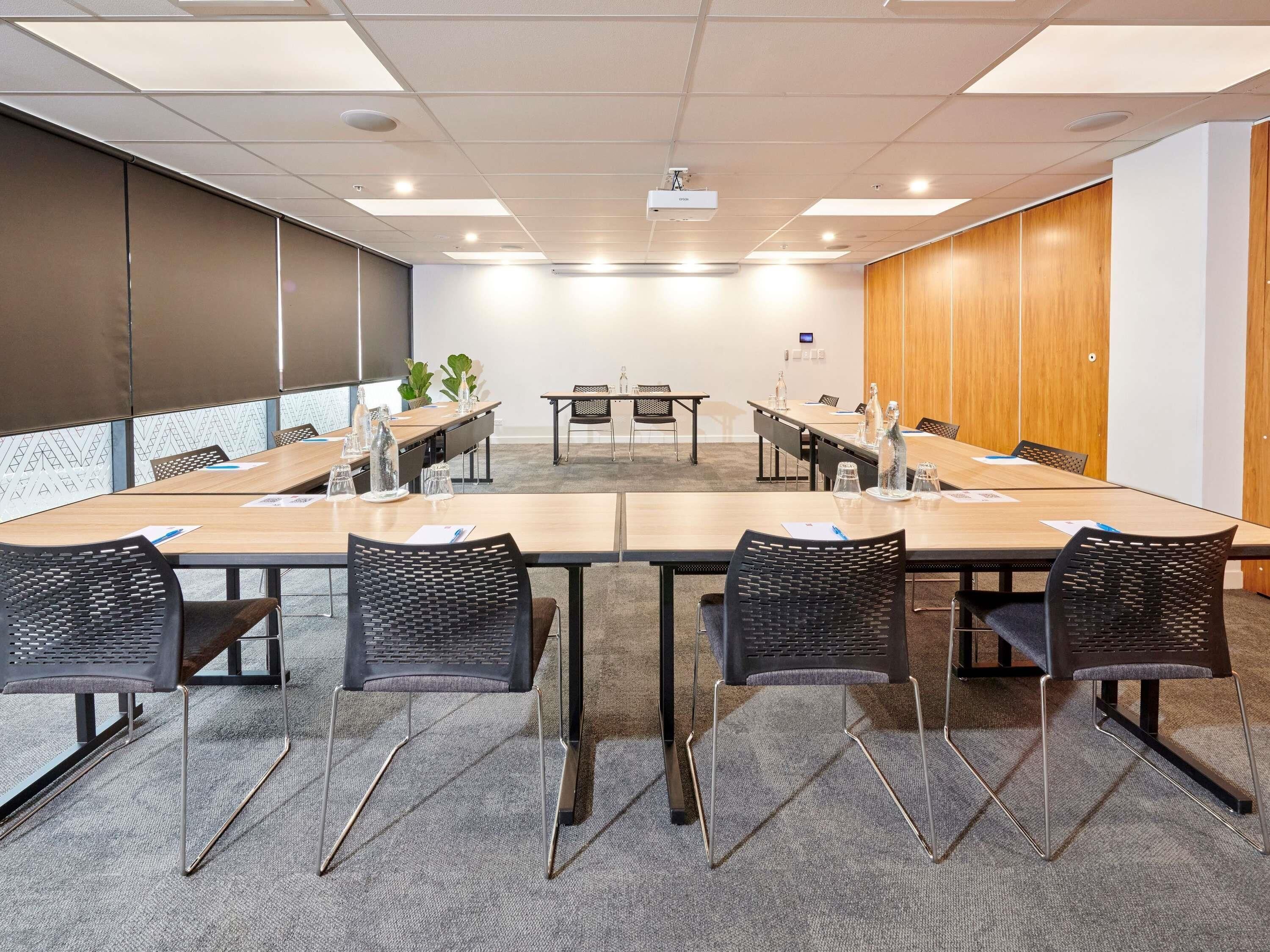 Une salle de conférence avec une longue table, des chaises, un projecteur et un mur recouvert de panneaux de bois.