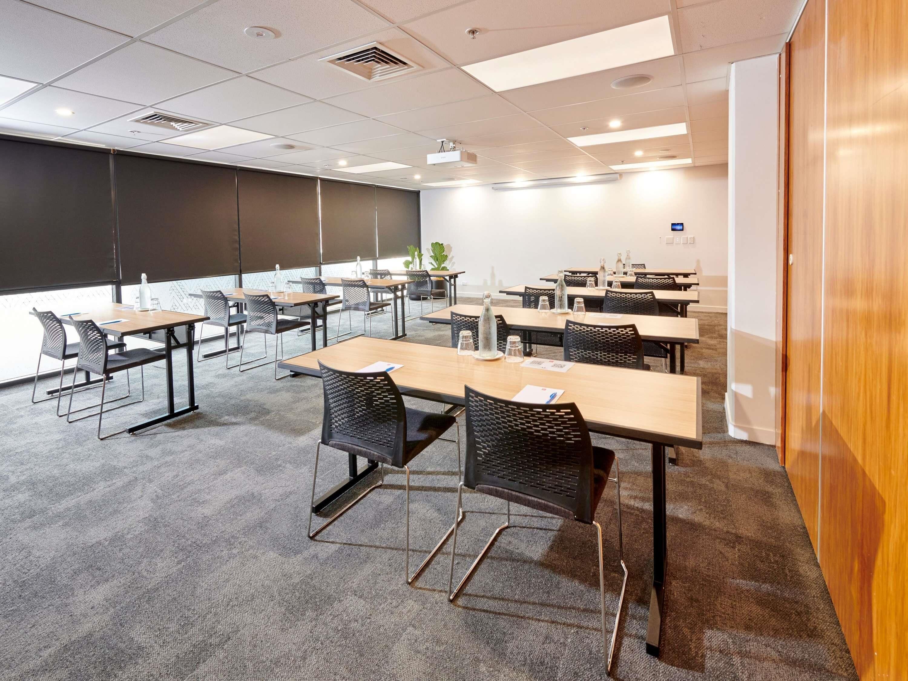 Una sala de conferències amb taules, cadires, una pantalla de projector i una pissarra.