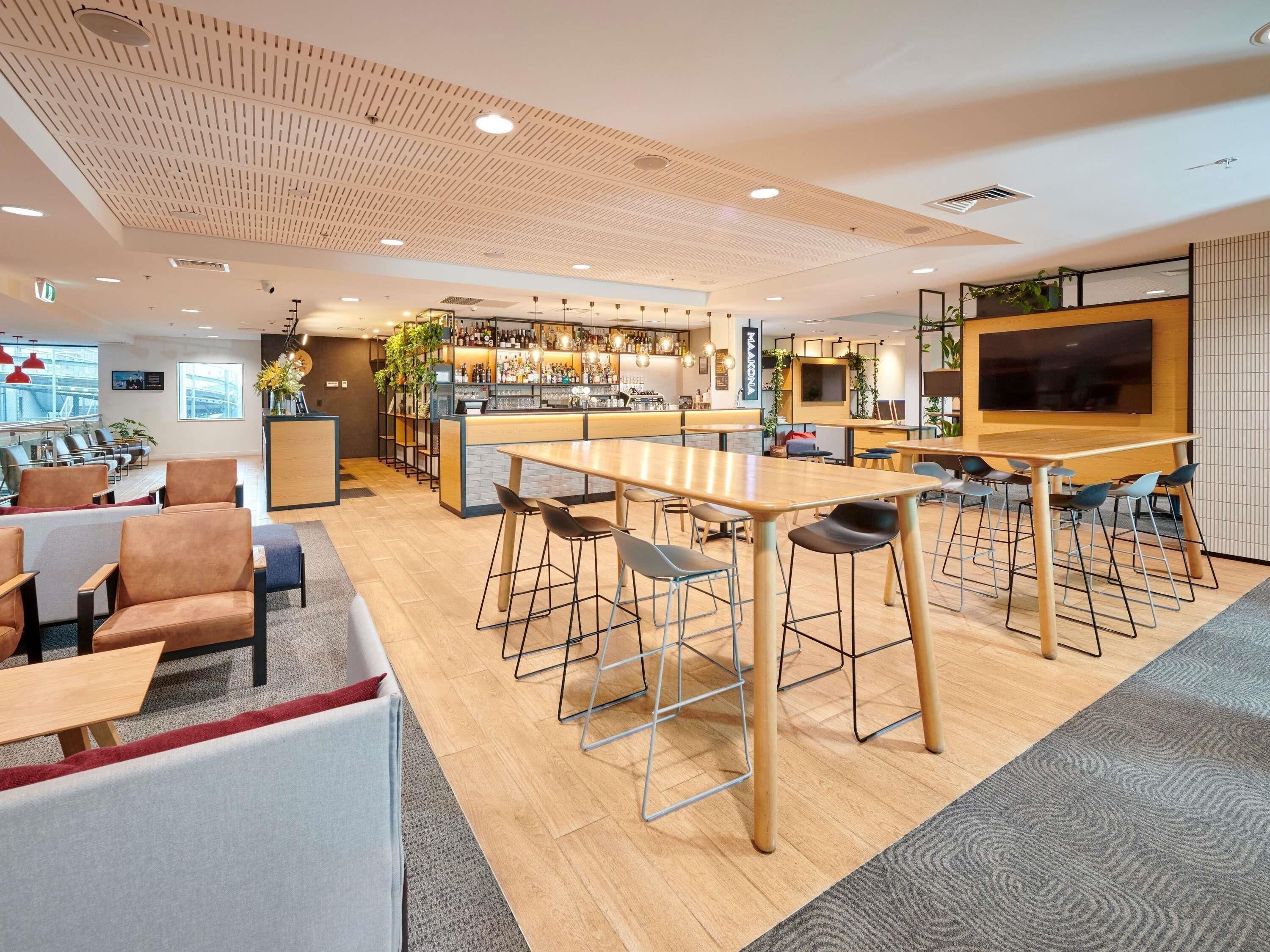 Zona de bar moderna con techo de madera, disposición de asientos y una pantalla grande.