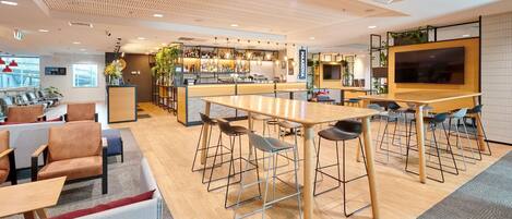 Zona de bar moderna con techo de madera, disposición de asientos y una pantalla grande.