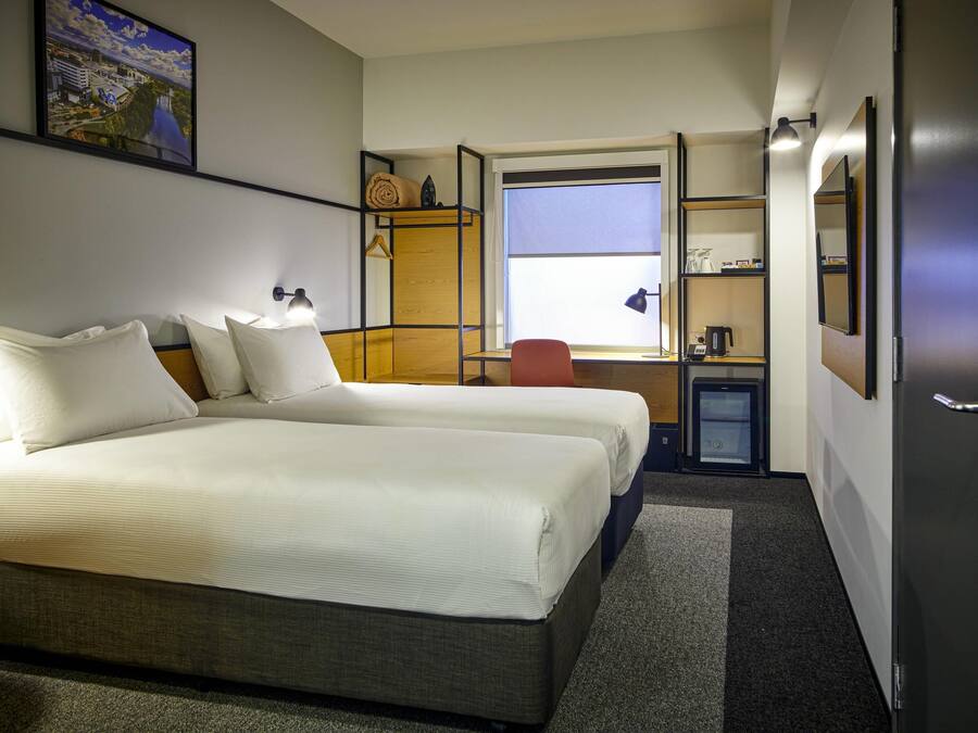 A hotel room with a large bed, a desk with a chair, a small kitchenette, and a window with a view of a bridge.