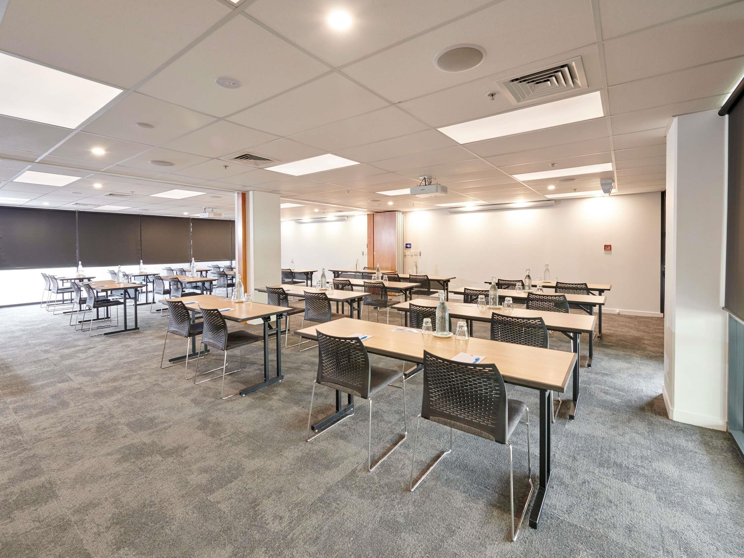 Una sala de conferències amb taules, cadires, una pantalla de projector i una finestra gran.