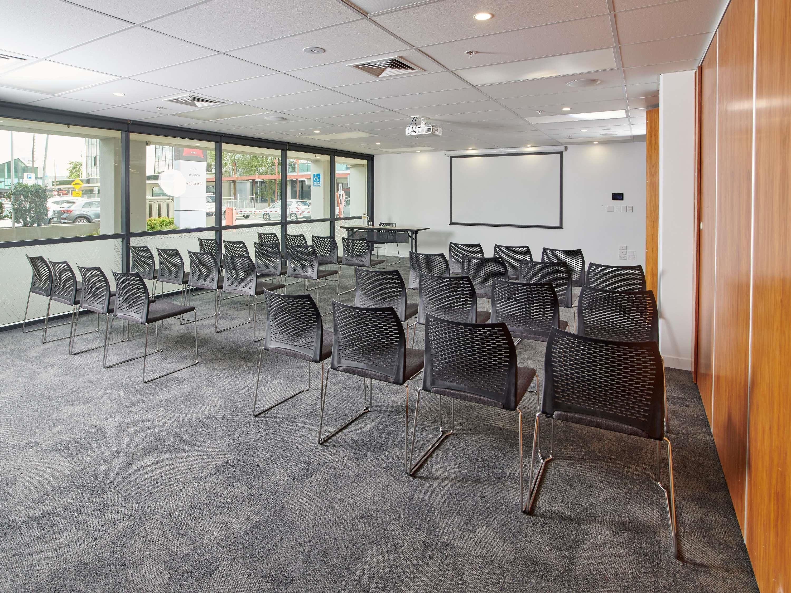 A conference room with rows of chairs, a projector screen, and large windows.